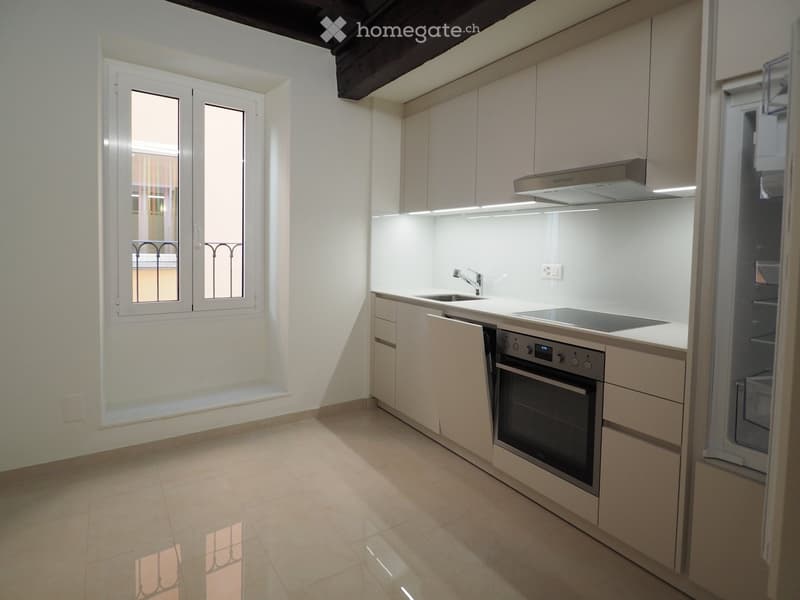 Modern kitchen with white cabinets, stainless steel appliances, and a large window with decorative iron bars.