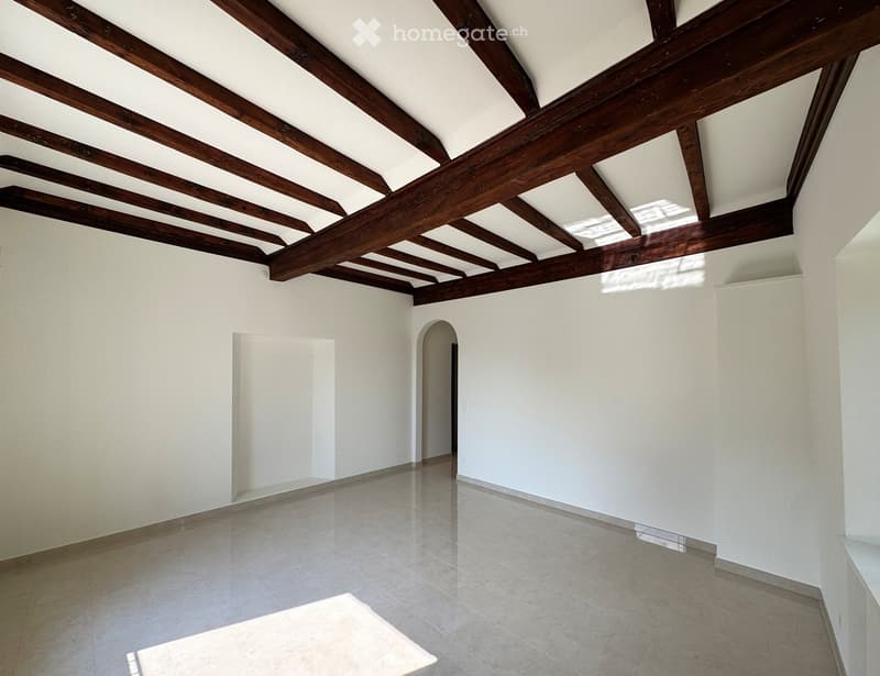 Empty room with white walls, exposed wooden ceiling beams, and tiled floor. No furniture or equipment visible.
