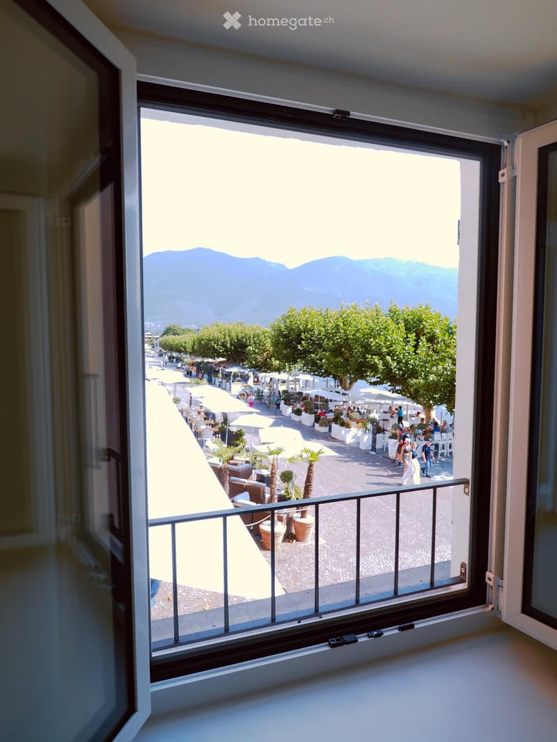 Balcony with a view of a scenic outdoor area featuring tables, chairs, umbrellas, and distant mountains.