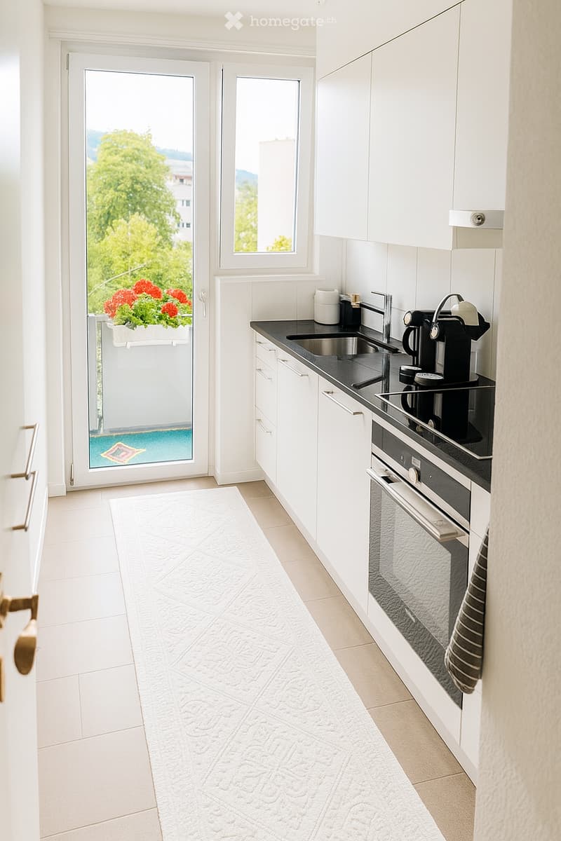 Modern kitchen with white cabinets, black countertops, stainless steel appliances, and a view of greenery through a large window and sliding door.