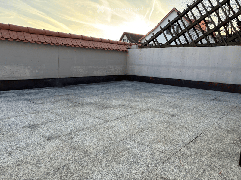 Empty rooftop terrace with concrete floor and low walls, featuring a wooden lattice structure in the background.