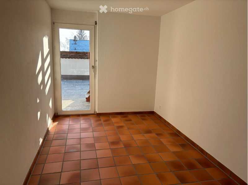 Empty room with tiled floor and white walls, featuring a door leading to an outdoor area.