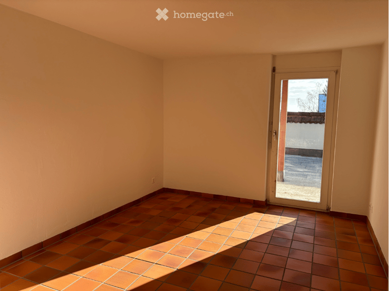Empty room with tiled floor and white walls, featuring a glass door leading outside.