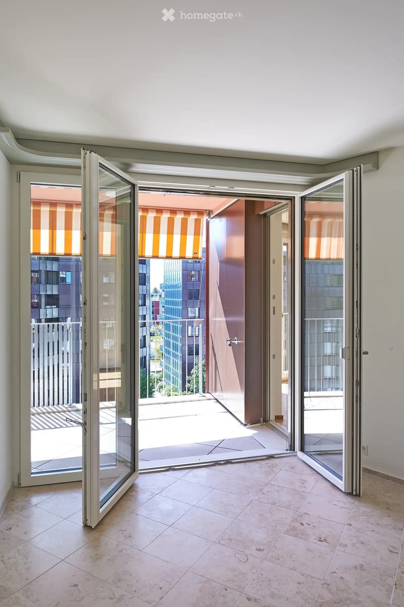 Open sliding doors lead to a balcony with a striped awning and a view of modern buildings.