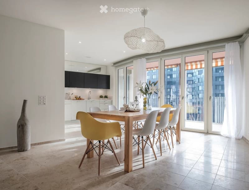 Modern dining area with a wooden table, white and yellow chairs, a large vase, and a kitchen area with cabinets and a sink.