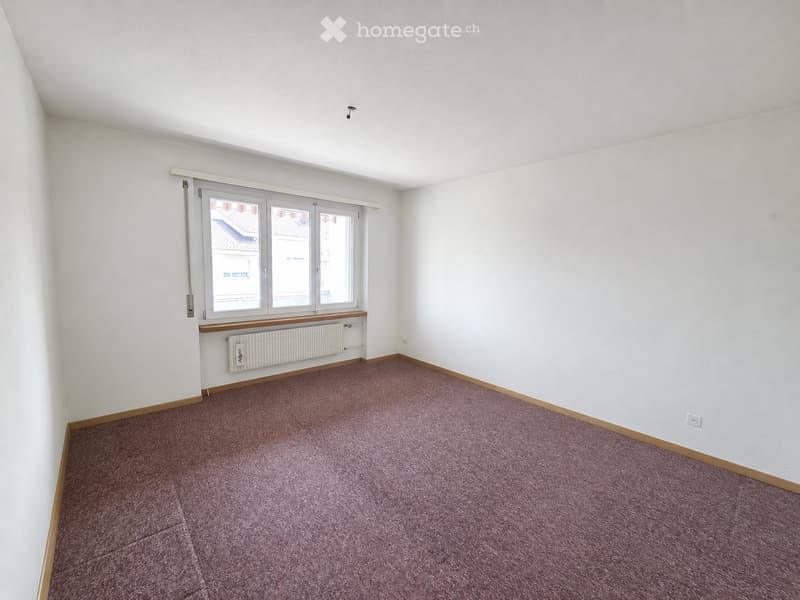 Empty room with white walls, purple carpet, and a window with a radiator below it.