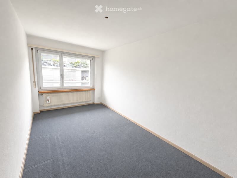 Empty room with light blue carpet, white walls, and a large window with a radiator below it.
