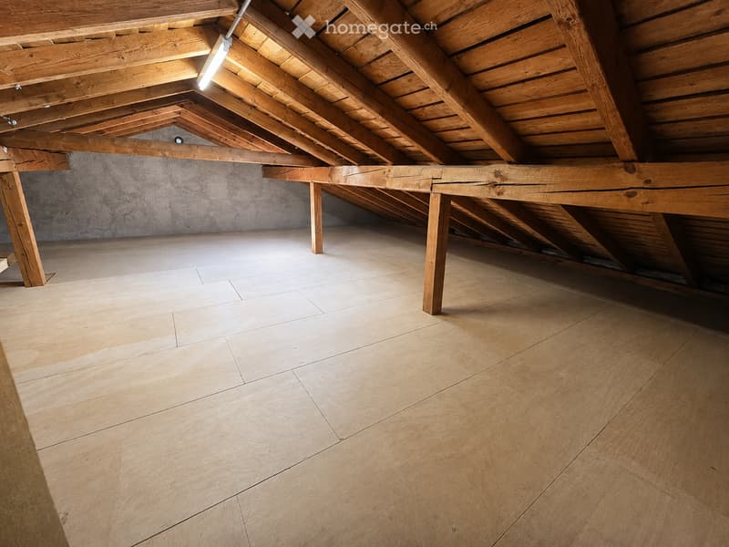 Empty attic space with wooden beams, exposed wooden ceiling, and tiled floor. No furniture or equipment present.
