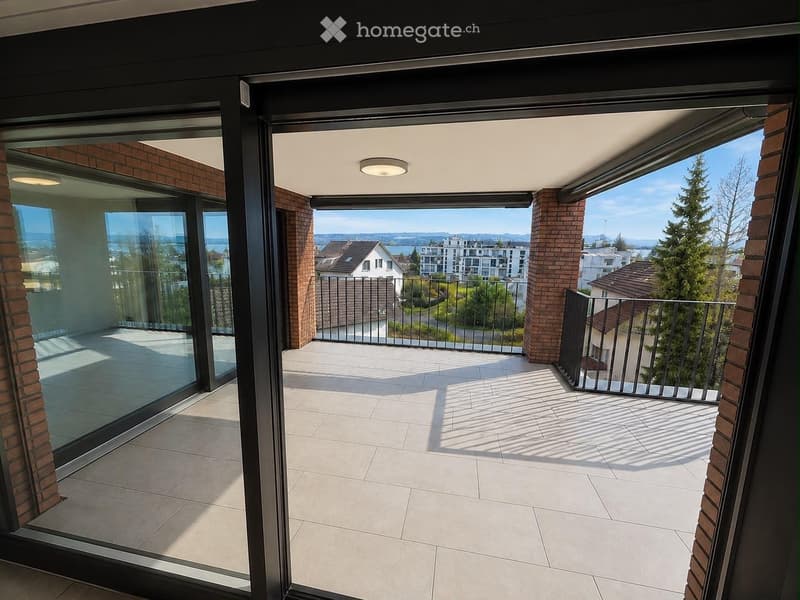 Spacious balcony with modern glass sliding doors, tiled floor, and metal railing, offering a scenic view of the city and surrounding landscape.