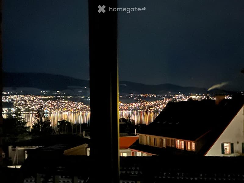 Nighttime view from a balcony showing a cityscape with numerous lights and a distant mountain range.