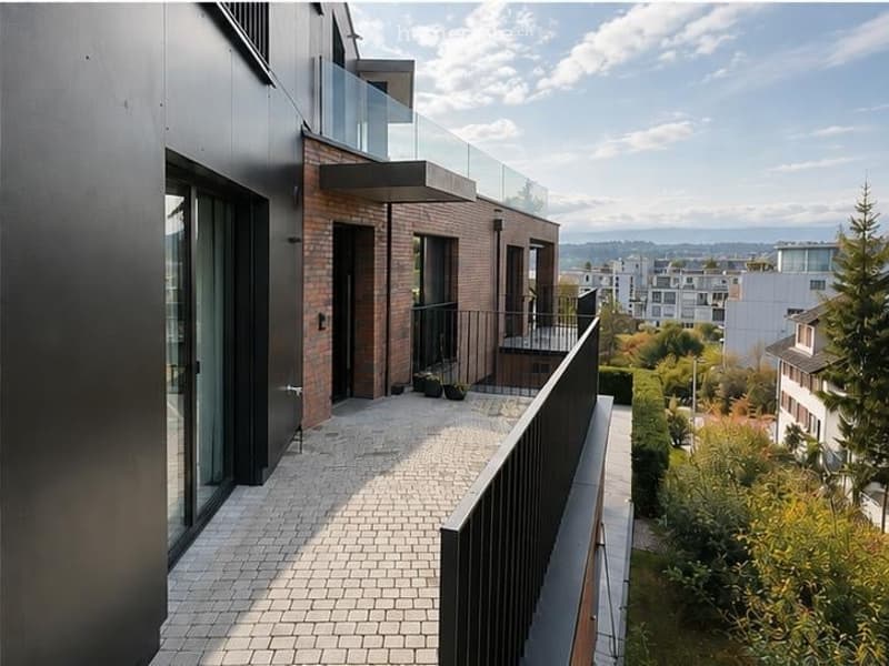Modern balcony with glass railing, tiled floor, and a view of the cityscape and surrounding greenery.
