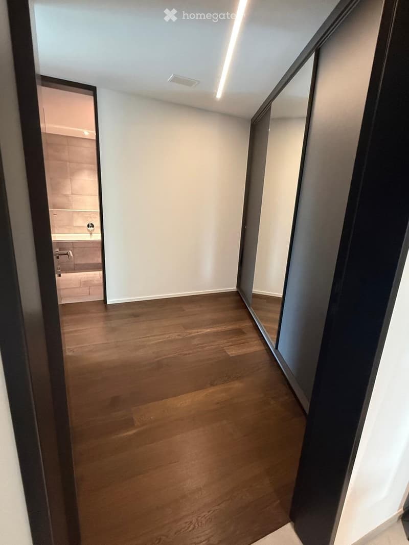Empty hallway with wooden flooring, white walls, and a partially open door leading to a bathroom.