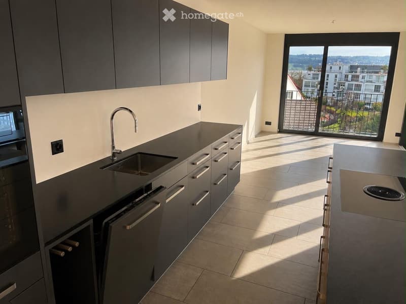 Modern kitchen with dark countertops, stainless steel appliances, and a large window offering a city view.