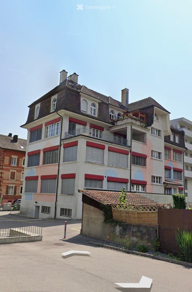 Multi-story residential building with red shutters, balconies, and a raised ground floor entrance.