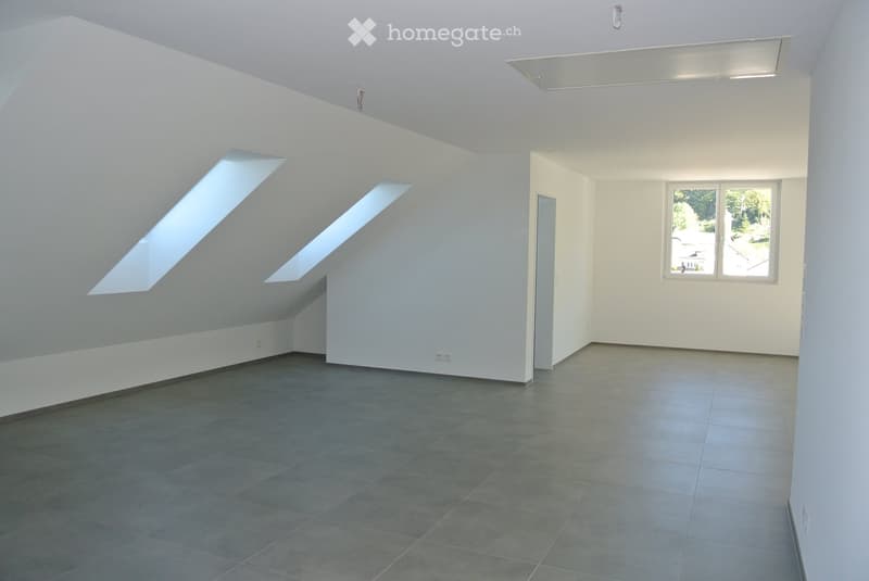 Empty room with white walls, grey tiled floor, and skylight windows providing natural light.