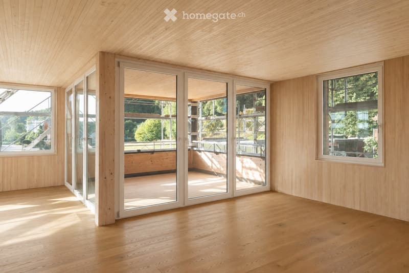 Completely empty room with wooden walls, wooden floor, large windows, and sliding glass doors leading to an outdoor area.