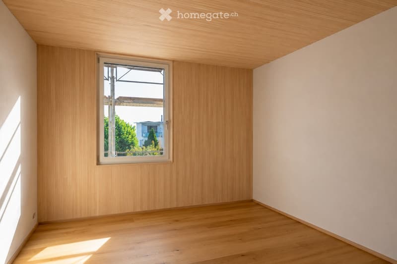 Empty room with wooden walls, wooden floor, and a single window showing a view of the outside. No furniture or equipment present.