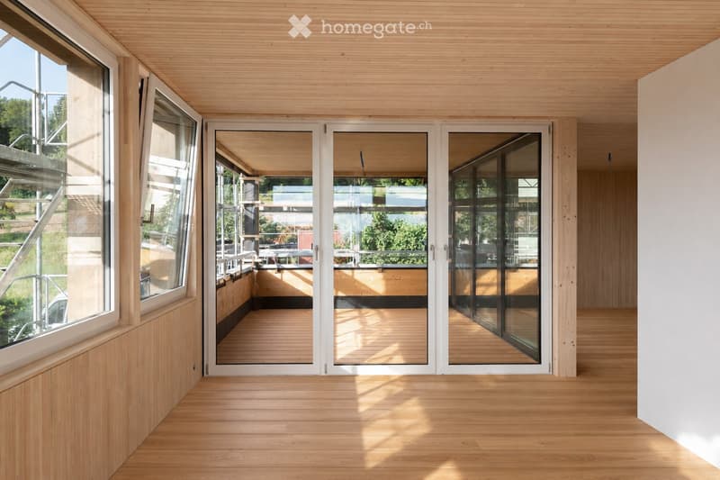 Bright, minimalist room with light wooden flooring and ceiling, large glass doors leading to an outdoor deck area.