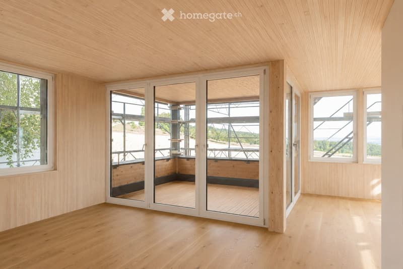 Empty room with light wooden walls and ceiling, large windows, and sliding glass doors leading to an outdoor deck.