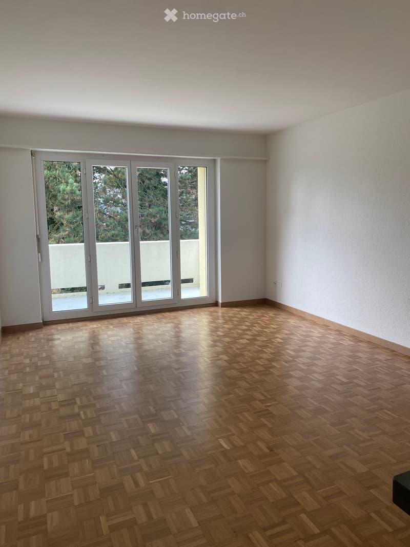 Empty room with wooden herringbone flooring, white walls, and large sliding glass doors leading to an outdoor area.