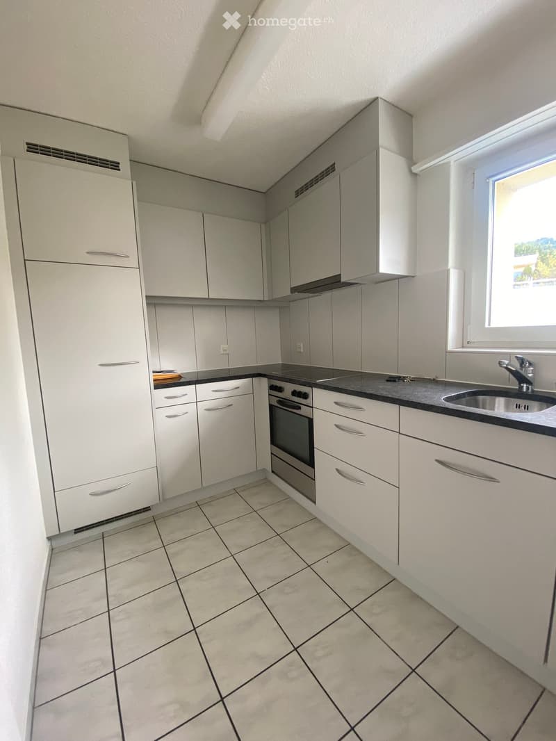 Modern kitchen with white cabinets, black countertops, and tiled flooring. Features include a refrigerator, oven, and sink.