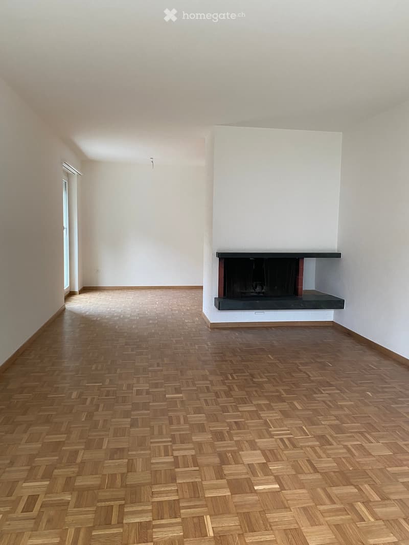Empty room with wooden herringbone flooring, white walls, and a built-in fireplace with a black mantelpiece.