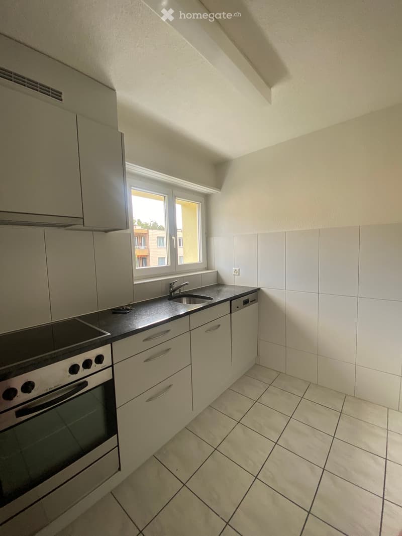 Modern kitchen with white cabinets, black countertop, built-in oven, sink, and faucet. The room features tiled flooring and a window offering a view of the outside.