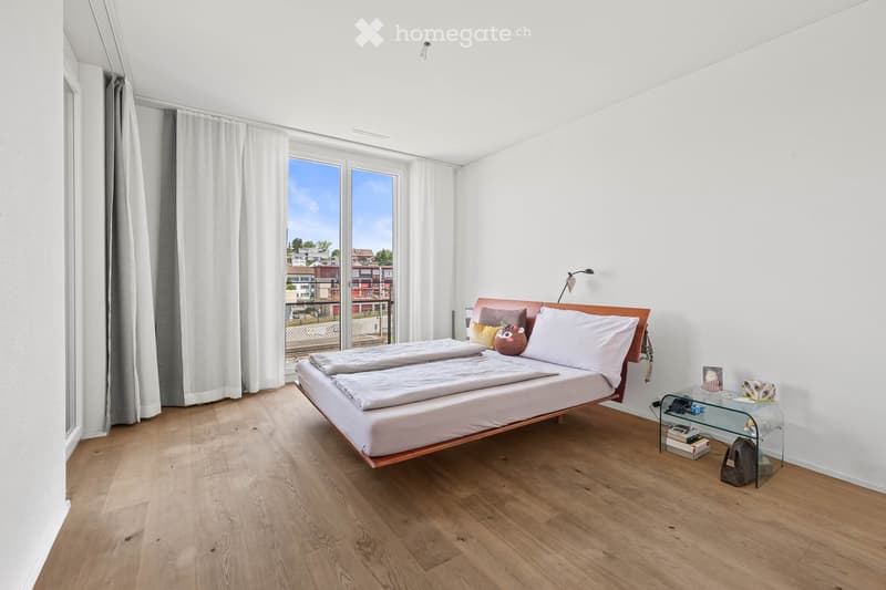 Modern bedroom with a wooden bed, white bedding, nightstand, and a view of the city through large windows.