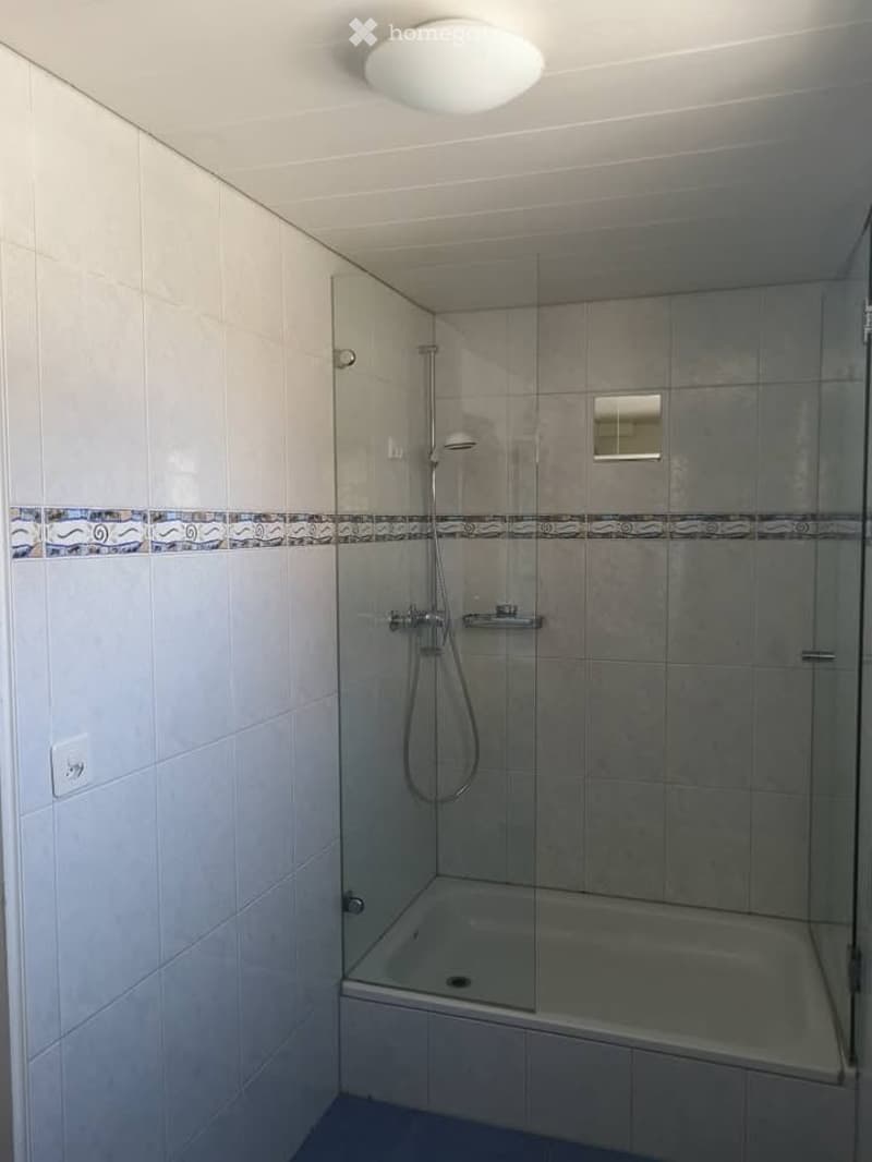 Modern bathroom with a bathtub, glass-enclosed shower, tiled walls, and a decorative border tile design.