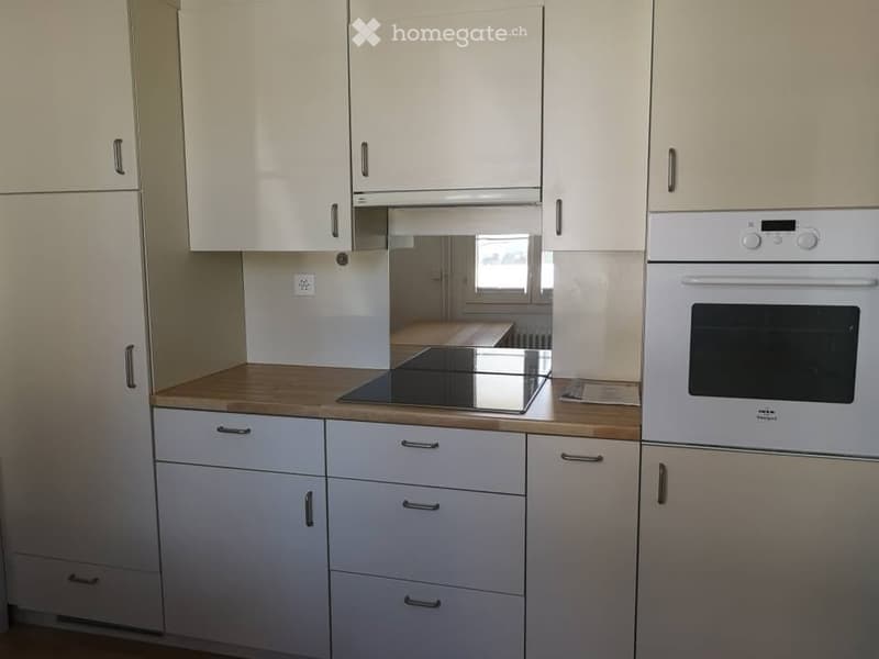 Modern kitchen with white cabinets, wooden countertop, induction cooktop, and built-in oven.