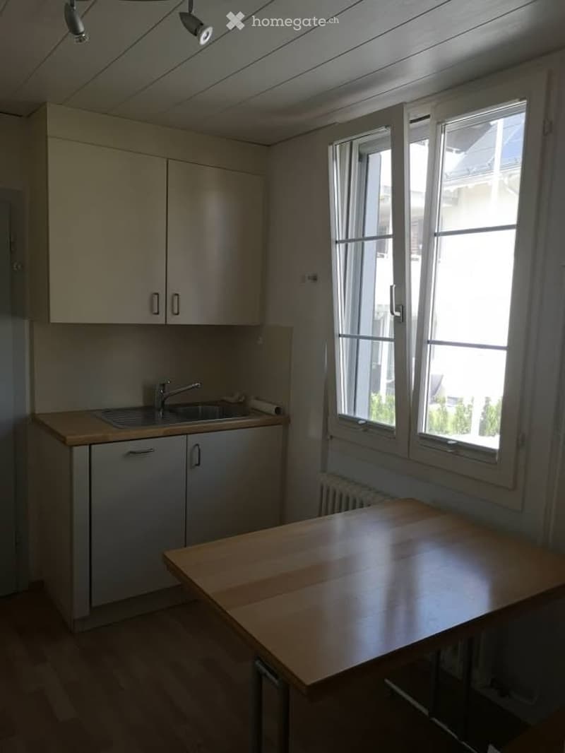 A small, unfurnished kitchen with a wooden table, sink, faucet, and cabinets.
