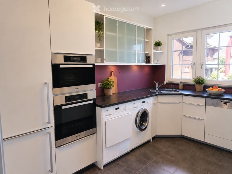 Modern kitchen with white cabinets, stainless steel appliances, dark countertops, and a window overlooking the street.