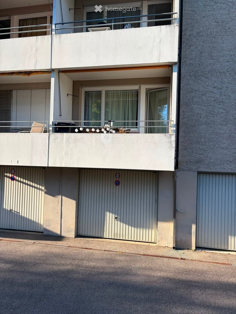 Two-story residential building with balconies, large windows, and a covered entrance area.