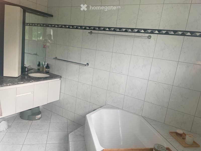 Modern bathroom with white marble tiles, a bathtub, a sink with a mirror, and a towel rack.