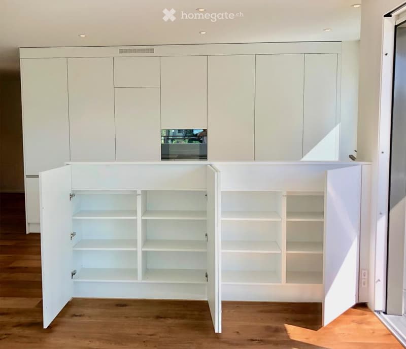 Empty room with white built-in cabinets and open shelving units, wooden flooring, and recessed ceiling lighting.