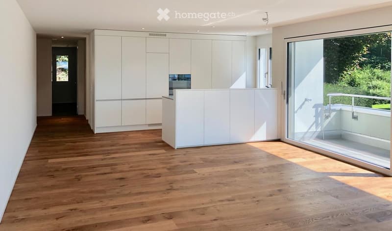 Bright, unfurnished room with wooden flooring, white cabinetry, and large glass sliding doors leading to a balcony.
