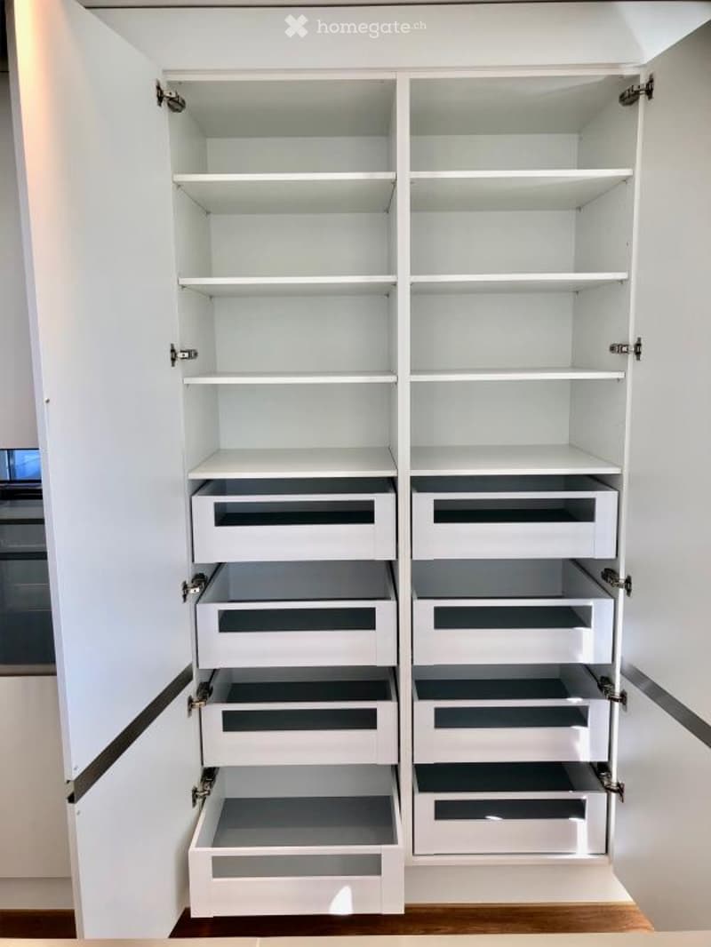 An empty, modern white pantry with multiple shelves and drawers, fully open and organized.