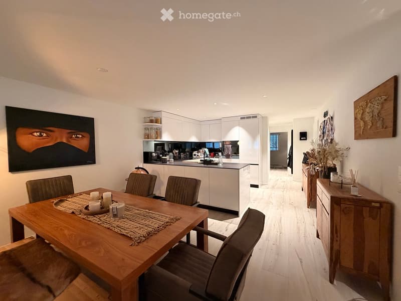 Modern dining area with a wooden table, four chairs, and a small kitchen area with white cabinets and a sink.