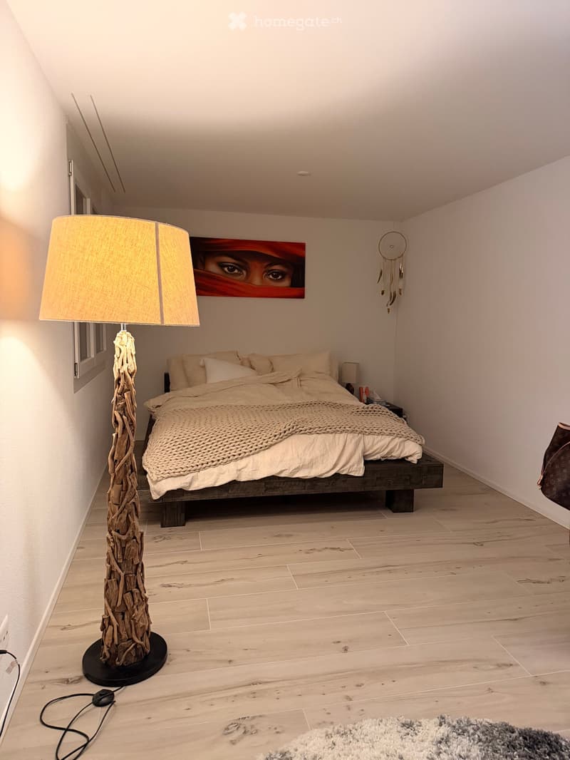 Modern bedroom with a wooden bed, nightstand, floor lamp, picture frame, dreamcatcher, and a rug on the floor.