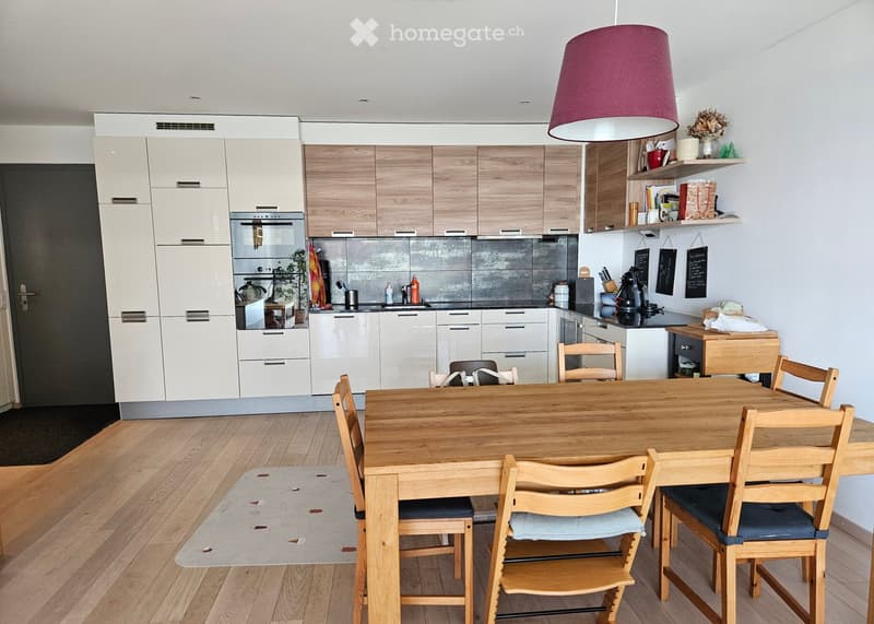 Modern kitchen with white and light wood cabinets, a wooden dining table with six chairs, and various kitchen appliances and utensils.