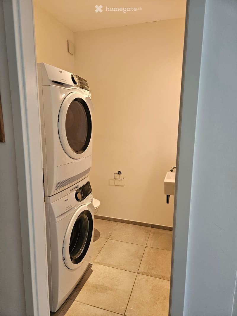 Bathroom with a stacked washing machine and dryer unit, a small sink, and tiled flooring.