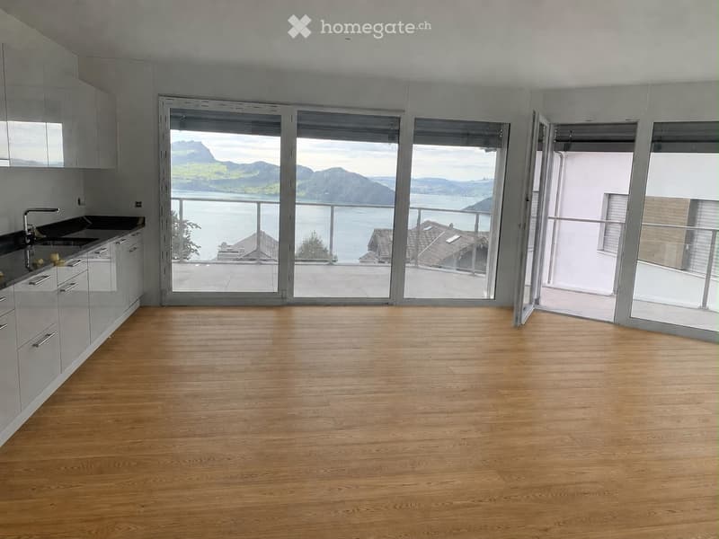 Empty room with wooden flooring, white cabinets, and large glass doors opening to a balcony with a scenic lake and mountain view.