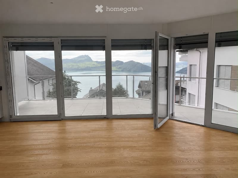 Empty room with wooden flooring and large glass doors leading to a balcony with scenic mountain and lake views.