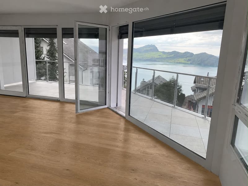Empty room with wooden flooring, large glass sliding doors leading to a balcony with a scenic mountain and lake view.