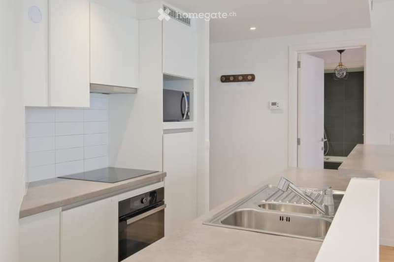 Modern kitchen with white cabinets, stainless steel sink, oven, microwave, and countertop.