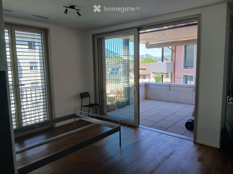 Bright living space with wooden flooring, large sliding glass doors leading to a tiled balcony, a modern chair, and a sleek table.