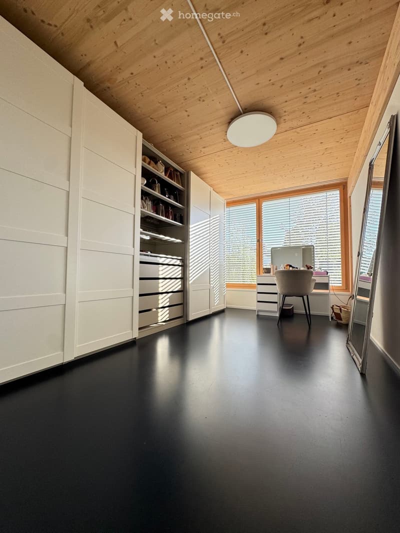Modern, minimalist room with a black floor, white wardrobe, large mirror, and a small desk area with a chair and lighting fixture.