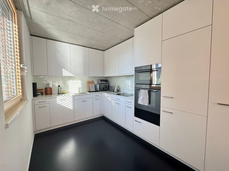 Modern kitchen with white cabinets, stainless steel oven, and black flooring.