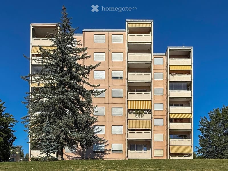 Multi-story residential building with beige facade, multiple windows, and balconies with striped awnings.