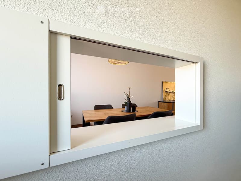 A modern dining area visible through an open sliding door, featuring a wooden dining table, chairs, a vase with flowers, and a picture frame on a side table.